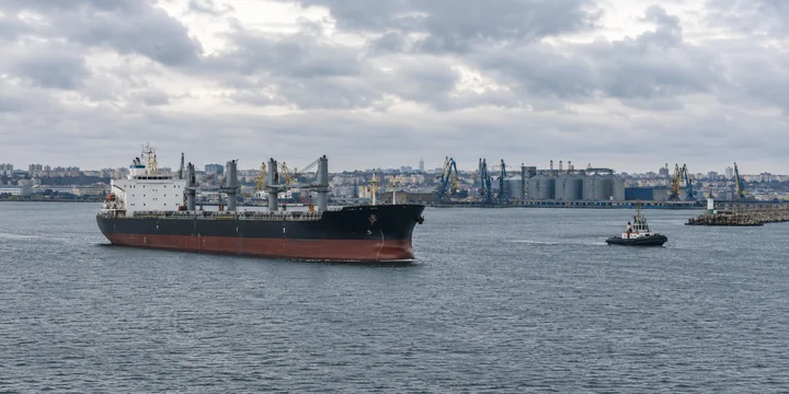 Bulk carrier and service boat in a harbor with cranes and grain silos behind
